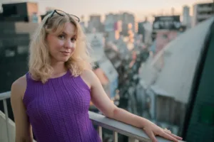 A woman in a purple dress leans on a rooftop railing, with the Tokyo cityscape in the background. Lifestyle portrait photography by JG.