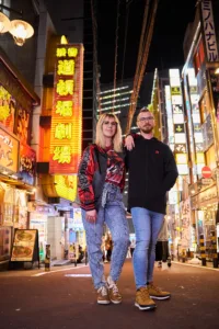 A couple posing for a professional portrait in front of the neon signs of the Shibuya Dotonbori Theater during a night photography tour in Tokyo.