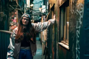 A person in a silver jacket poses in a narrow alleyway of Golden Gai, Shinjuku, Tokyo. Urban street portrait with graffiti and moody lighting.