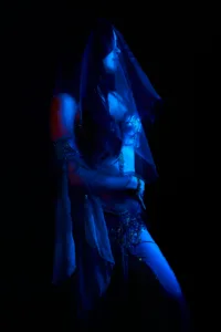 青い光に包まれたベールと装飾的な衣装を身にまとった女性のローキー・クリエイティブ・ポートレート。プロフェッショナルなスタジオライティング技術を強調しています。