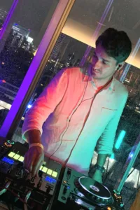 東京のライブ会場でライブセットを披露するフォトグラファー兼DJのJG。窓越しに都会の夜景が見える。