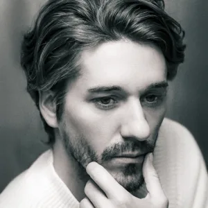 顎に手を当てて考え込むような表情を浮かべる、フォトグラファーJGのモノクロ・クローズアップ。ハイエンドかつシネマティックな美学が漂う一枚。