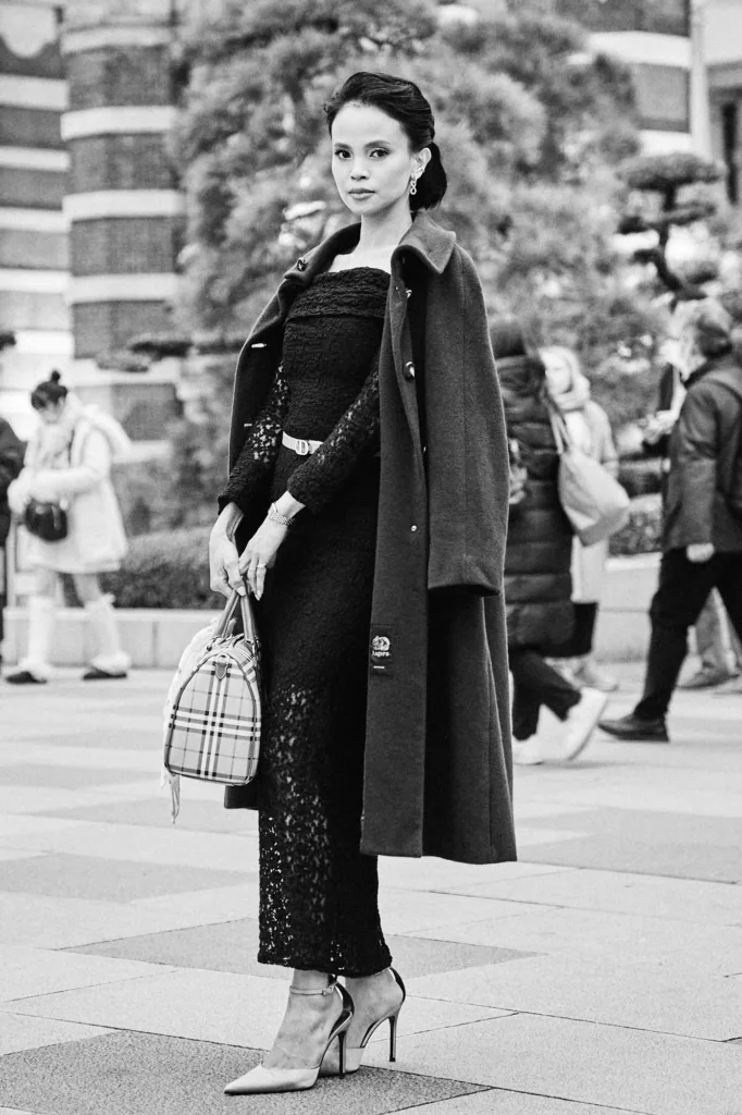 Elegant woman in a black lace dress with a coat over her shoulders posing in a Tokyo plaza, black and white editorial by JG.