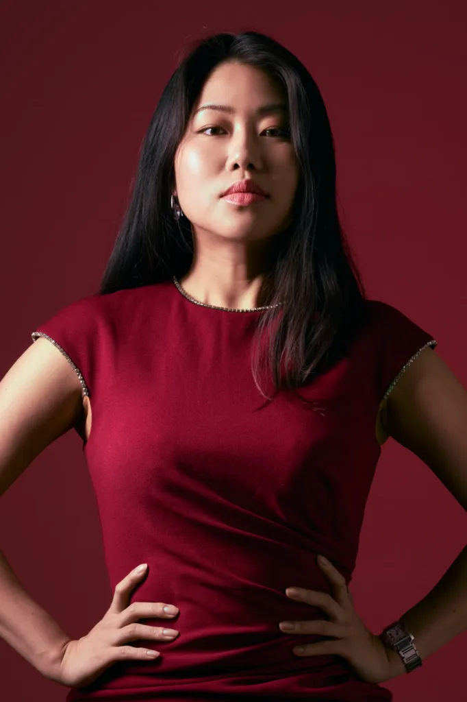 Model in a burgundy dress with rhinestone trim, hands on hips against a matching deep red backdrop, photographed at the Shibuya studio.