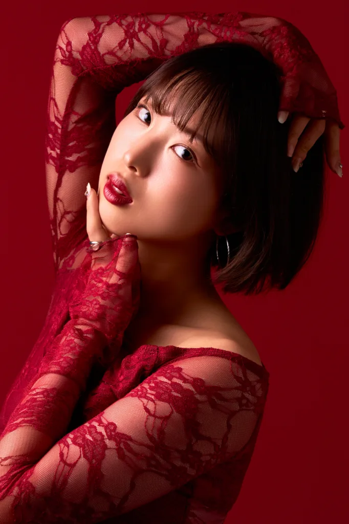 Model in a sheer red lace top with one arm raised, photographed against a matching deep red backdrop at the Shibuya studio.